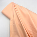 A bolt of peach colored fabric laying on a white table.