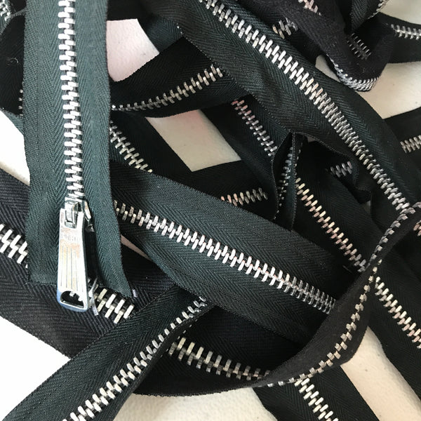 black metal zippers laying in a scattered pile on a white background