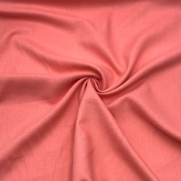 A close-up of linen/tencel blend fabric in a warm coral color. The fabric is scrunched into a swirl in the middle to show how it moves and folds. 