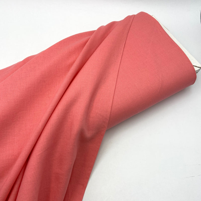 A bolt of bright warm coral pink fabric on a white table. 