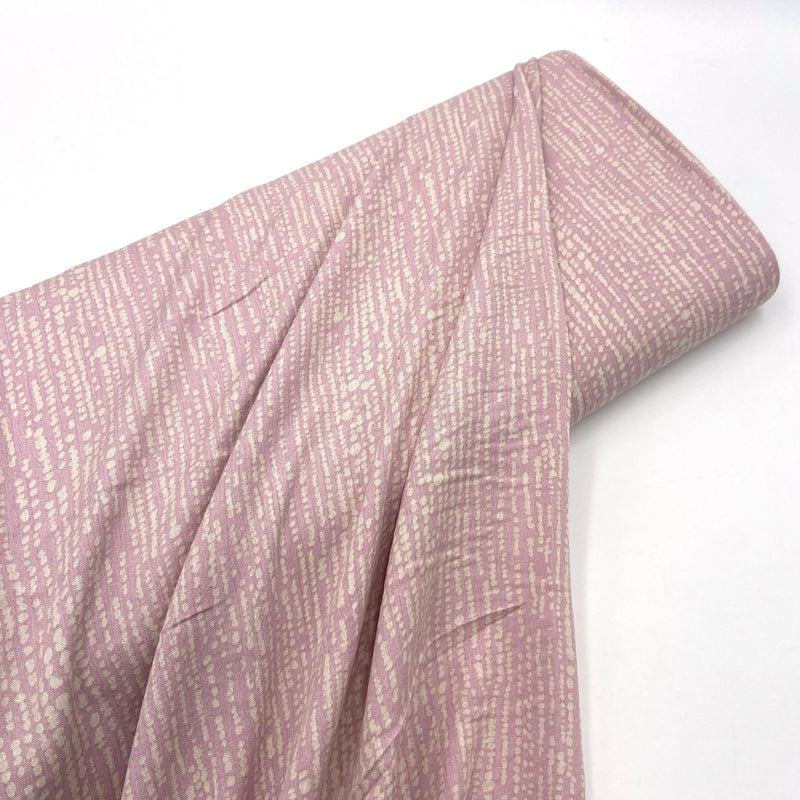 A bolt of pinkish purple fabric with a white abstract design on a white table.