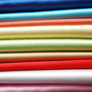 A stack of various colored bridal satin fabrics, ranging from blue, green, yellow, red, pink, to white.