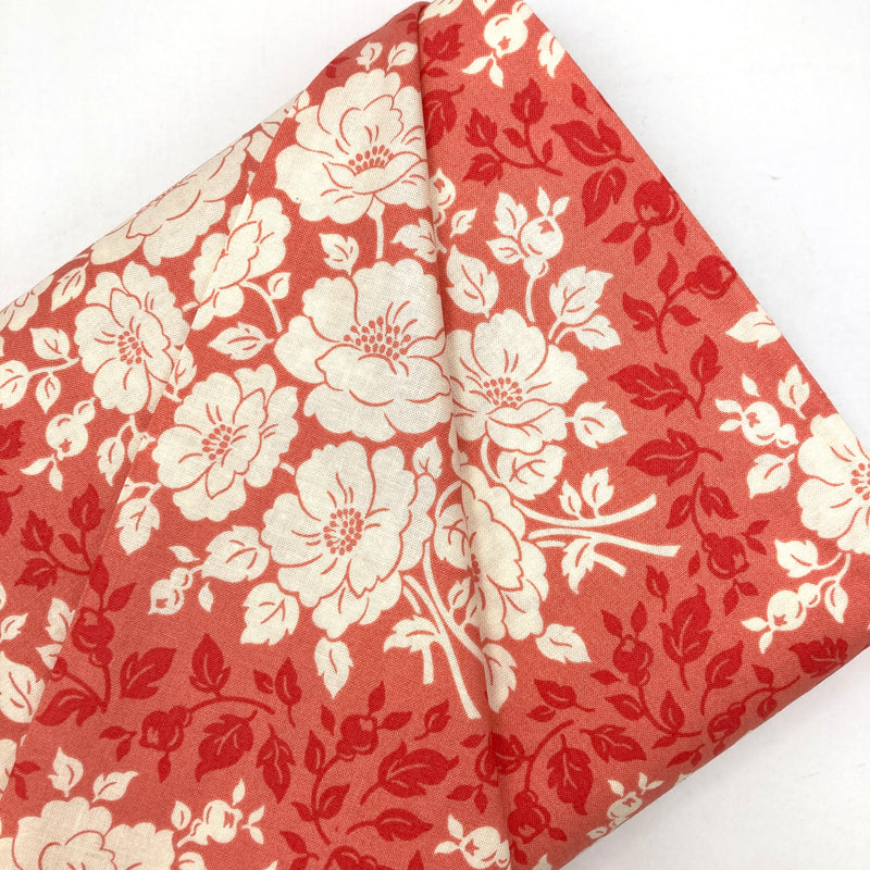 A bolt of coral pink quilting cotton with ivory flowers and vine designs.