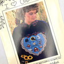 A photo of a woman wearing a sweatshirt with applique patterns including a heart, sunflower, sunhat, and various farm animals on it.