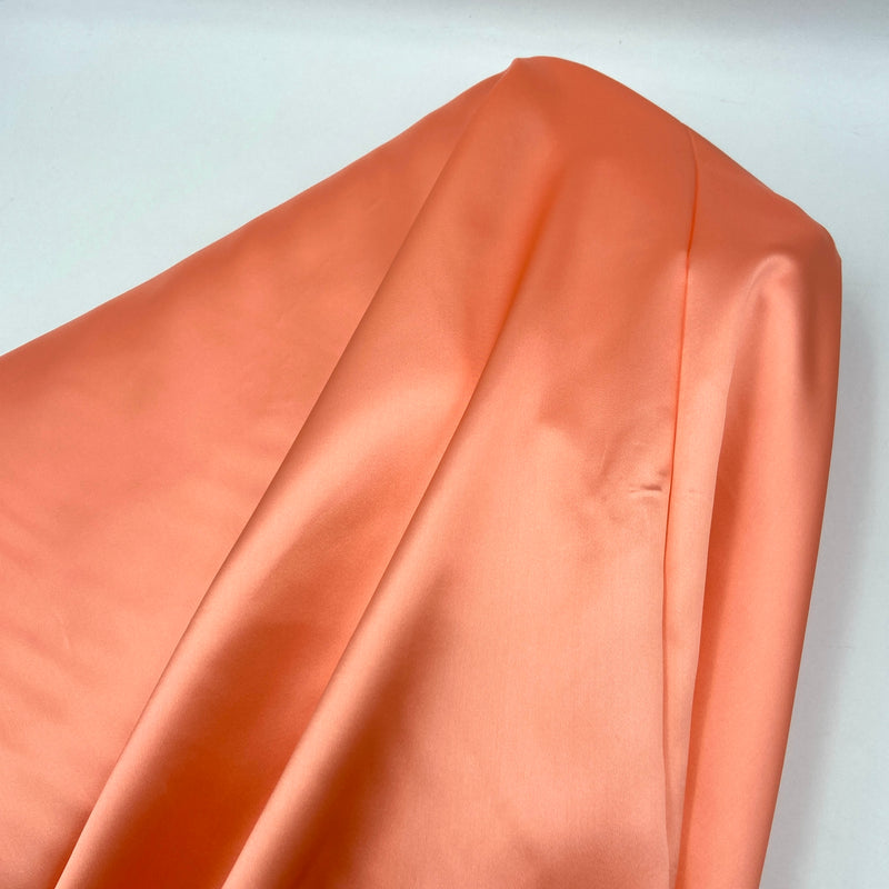 A bolt of bright salmon-colored satin fabric.