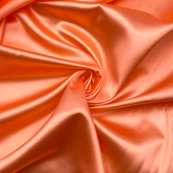 A firey coral-colored satin fabric that has been scrunched into a swirl in the middle, which accentuates the fabric's sheen. 