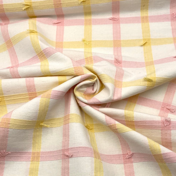 A white fabric with yellow and pink woven plaid stripes and decorative clipped threads. 