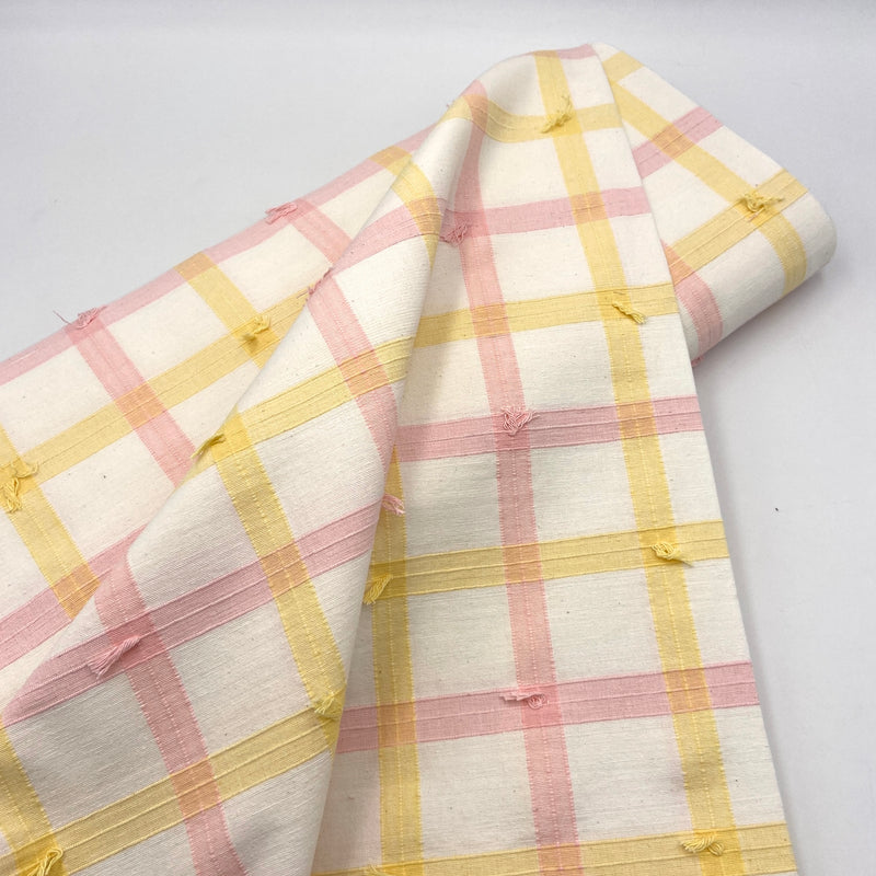 A bolt of white, pink, and yellow plaid fabric with tufts of clipped decorative threads. 
