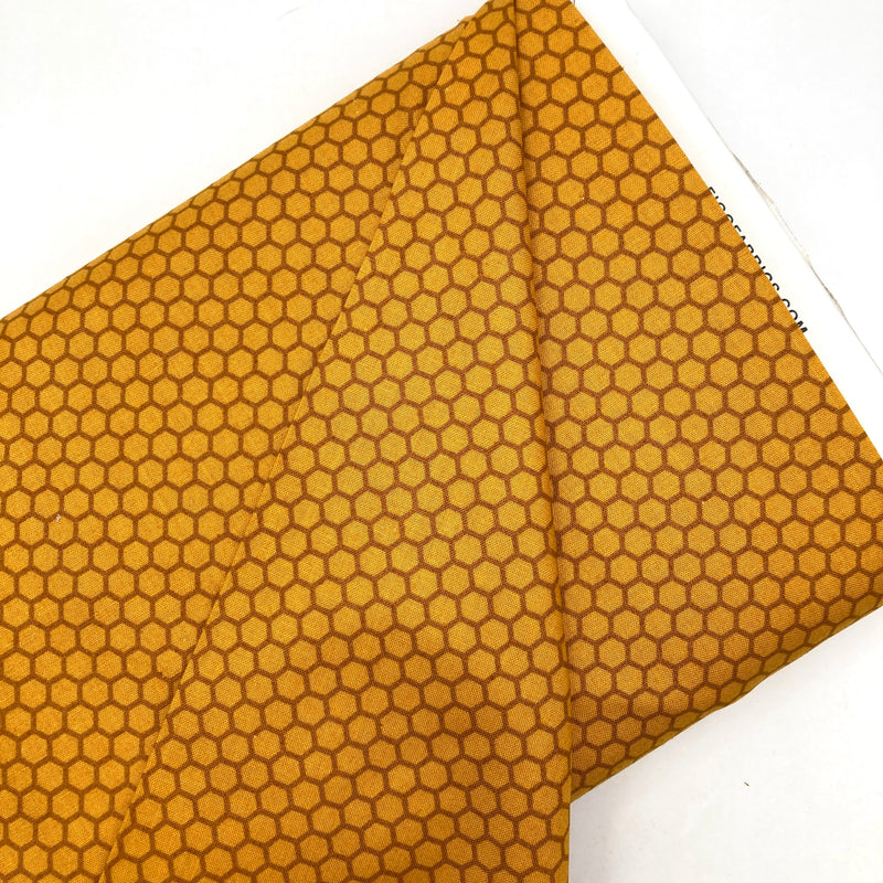 A bolt of quilting cotton fabric with a honeycomb design in honey yellow and brown shades. 