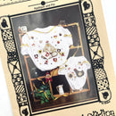 A photo of a sewing pattern package for a white fabric with applique designs, featuring images of chickens and pins. The package has a vintage appearance with a textured background and decorative borders.