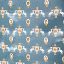 PUL fabric with A repeating pattern of whimsical unicorn and shield motifs on a dusty blue background, with white unicorns, peach and orange shields, and small illustrated faces inside ovals.
