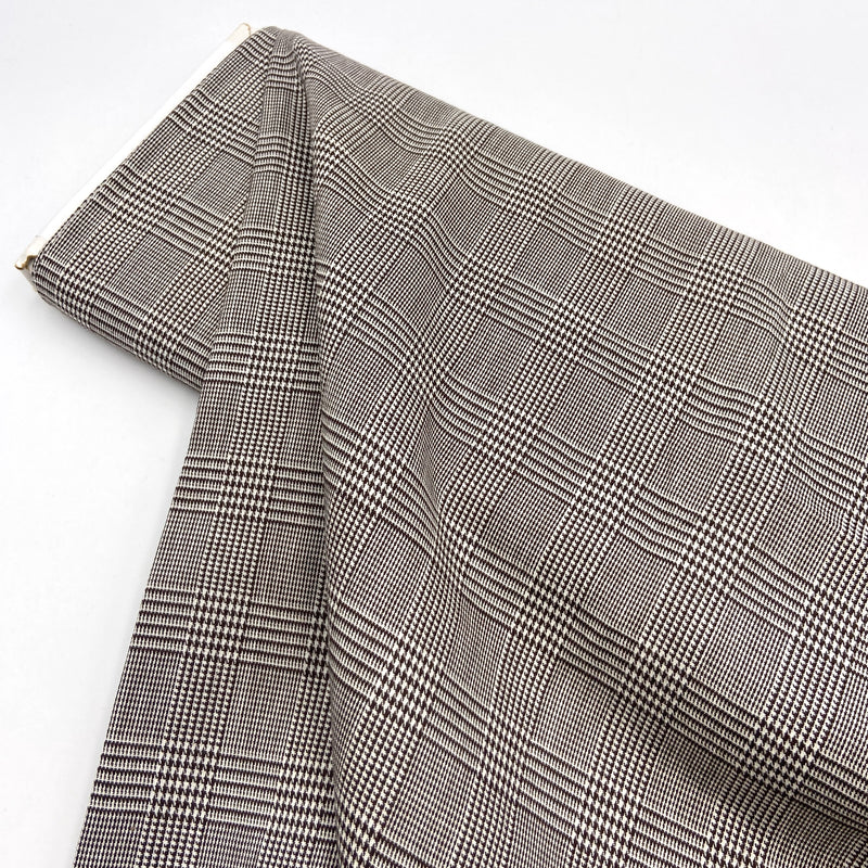 A bolt of houndstooth plaid polyester suiting fabric laying on a white table.