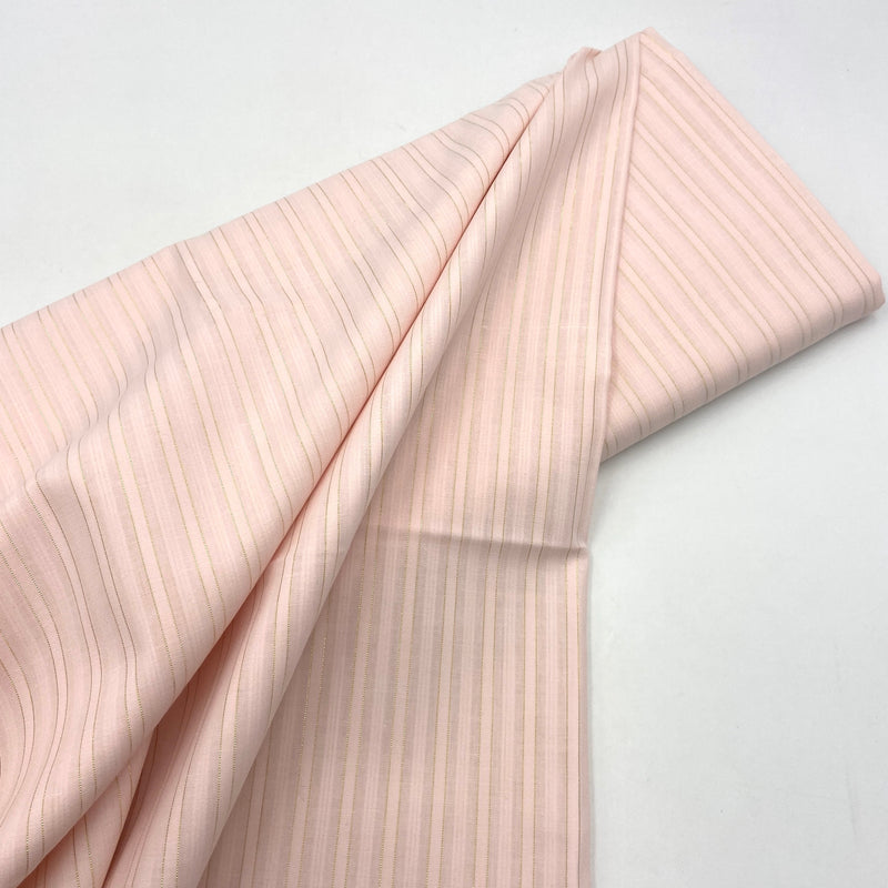 A bolt of pink shirting fabric with subtle gold stripes, laying on a white table. 