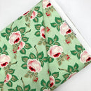A bolt of quilting fabric with a mint green background and soft pink florals. 