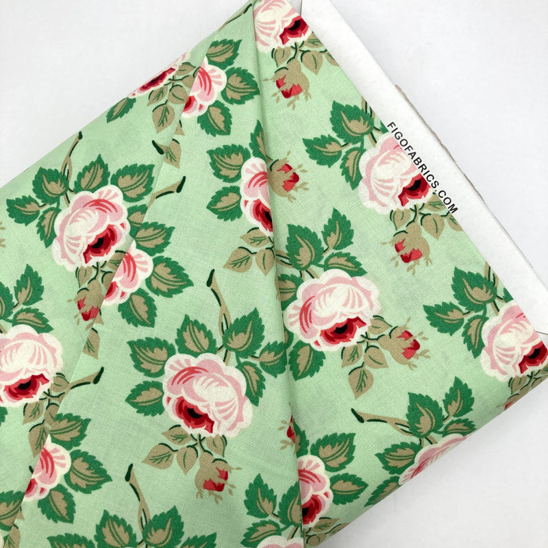 A bolt of quilting fabric with a mint green background and soft pink florals. 