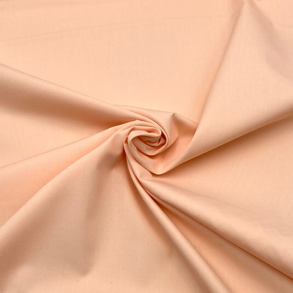 A light peach colored fabric scrunched in the middle to show how it folds and moves. 