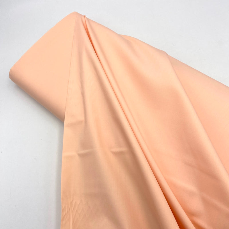 A bolt of peach colored fabric laying on a white table. 
