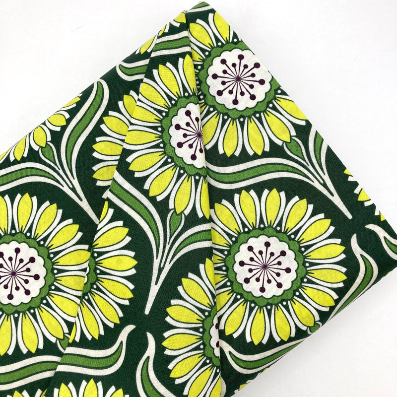 A bolt of quilting cotton with bold yellow flowers on a dark green background.