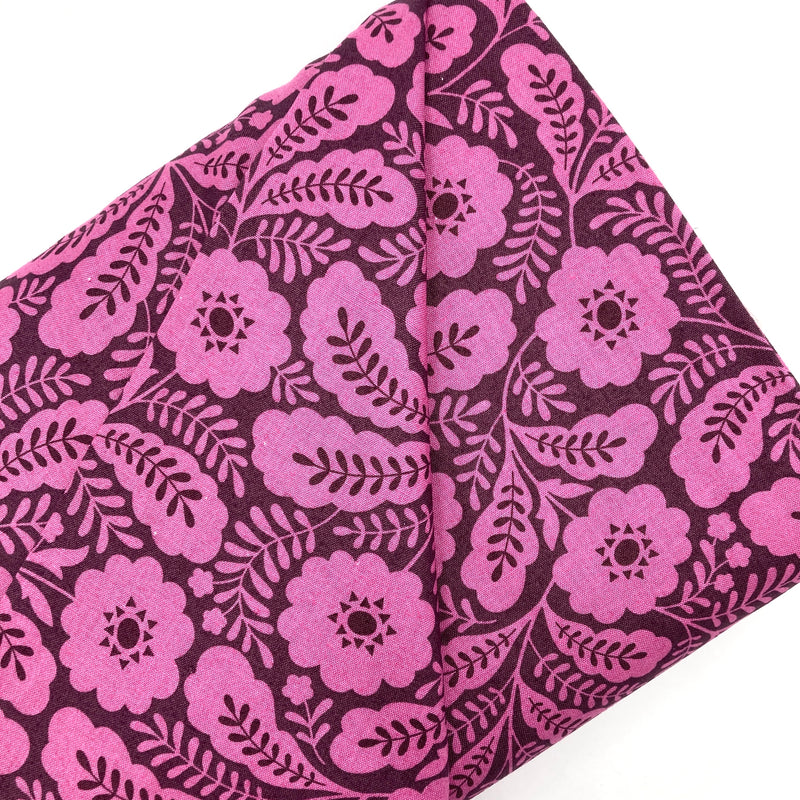 A bolt of quilting cotton fabric with a geometric floral design in a lilac color on a darker purple background.