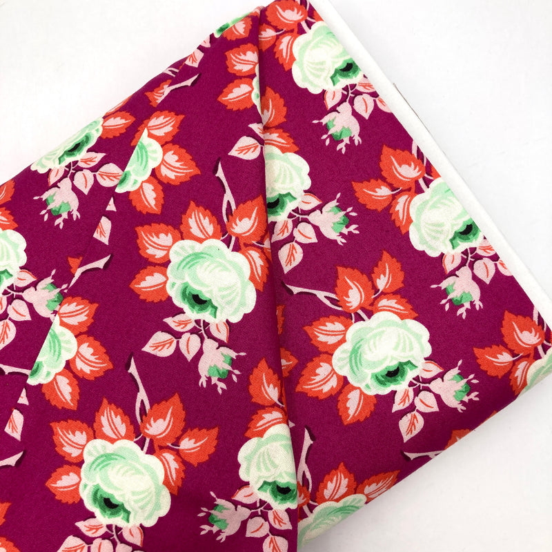A bolt of quilting fabric with a bold floral design in magenta, red, and green.