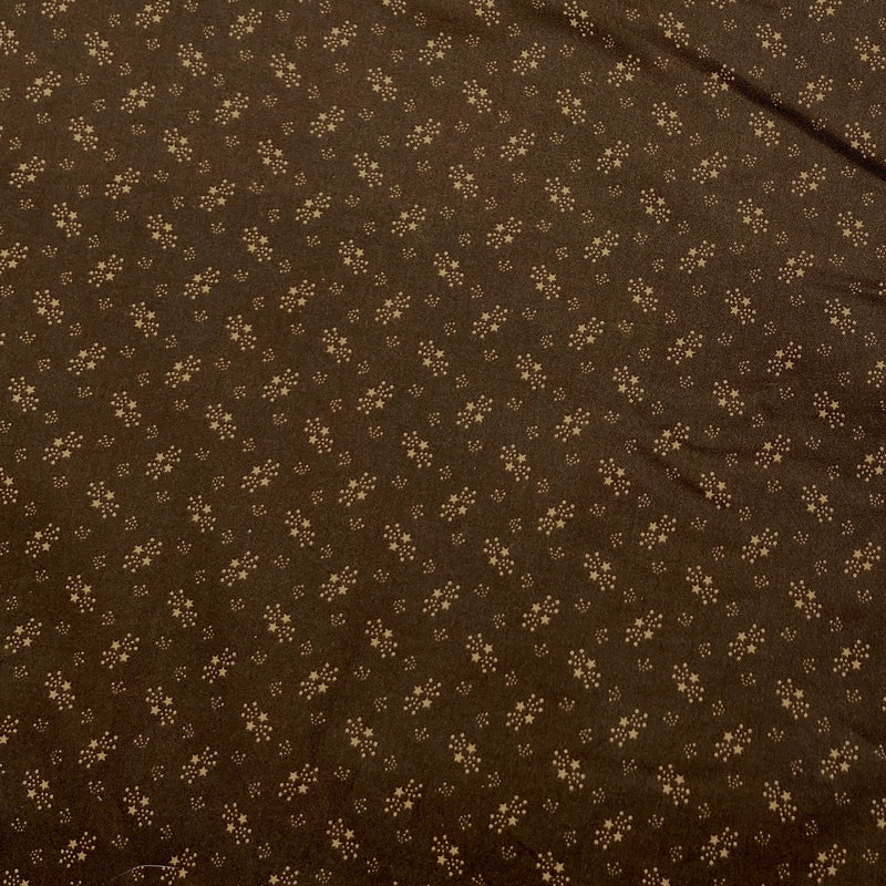 Cotton fabric with dot and star motifs in tan on a chocolate brown background.