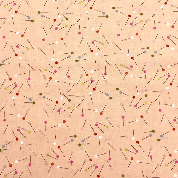 a quilting fabric with a design of scattered pins on a pale peach background