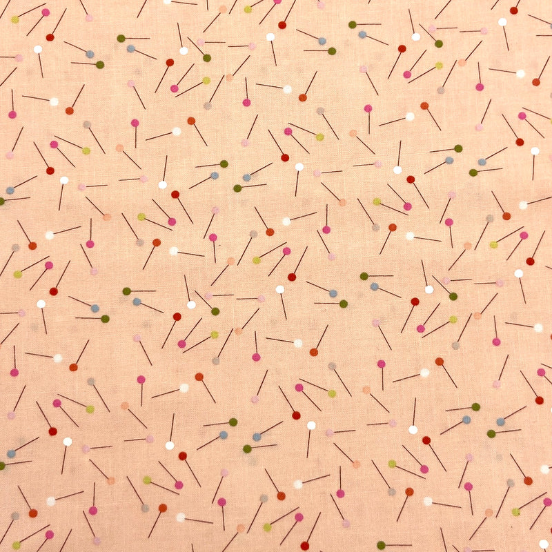 a quilting fabric with a design of scattered pins on a pale peach background