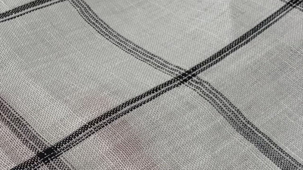 a video showing a close-up of the drape and opacity of a white linen fabric with a black plaid design