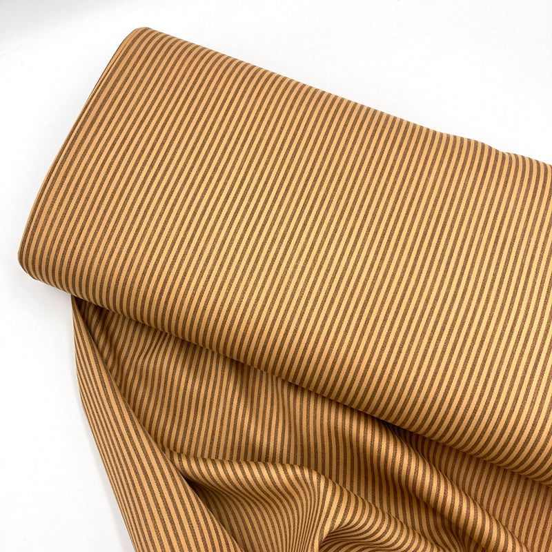 A bolt of yellow and brown striped cotton sateen fabric laying on a white table 