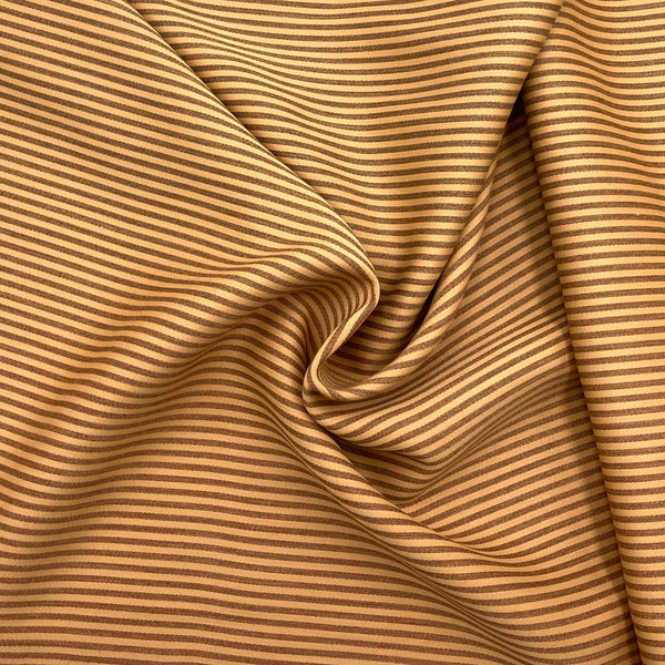 gold and brown striped cotton sateen fabric scrunched in a swirl pattern to show the fabric's thickness and drape qualitites