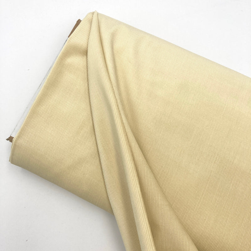 a bolt of light yellow corduroy fabric laid on a white table