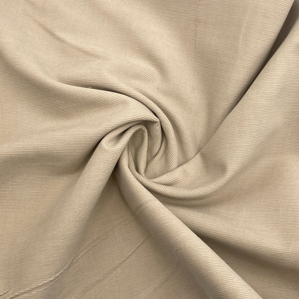 A greyish beige corduroy fabric scrunched in a swirl to show the texture of the fabric