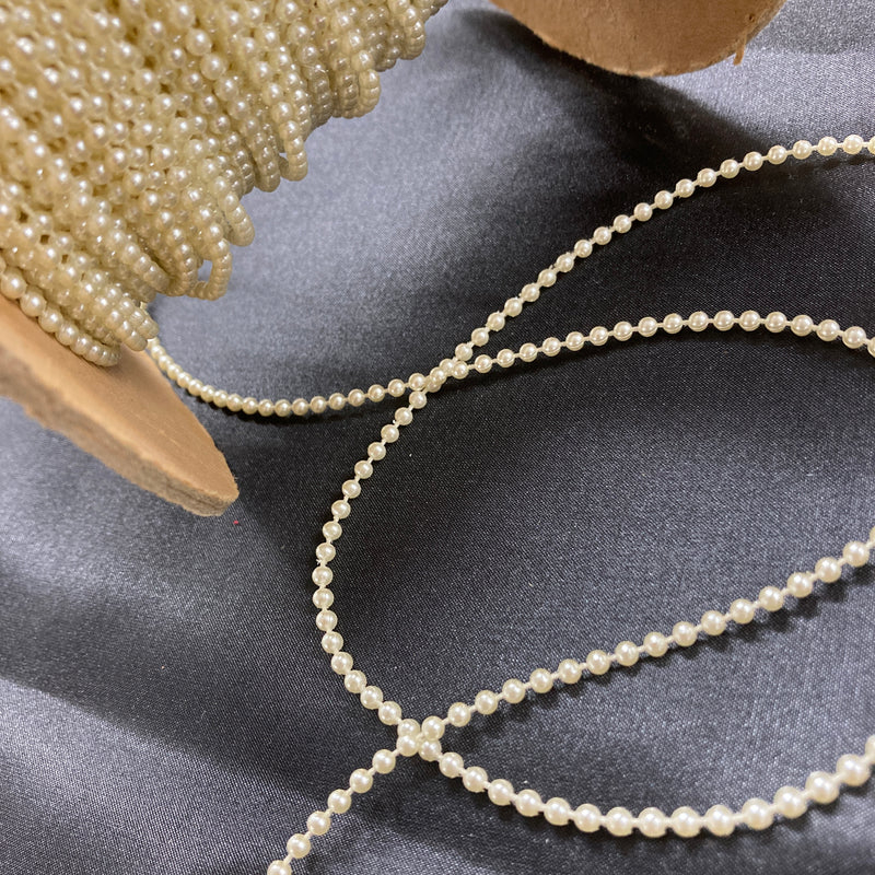 A roll of ivory-colored plastic pearl trim laying on a black piece of fabric