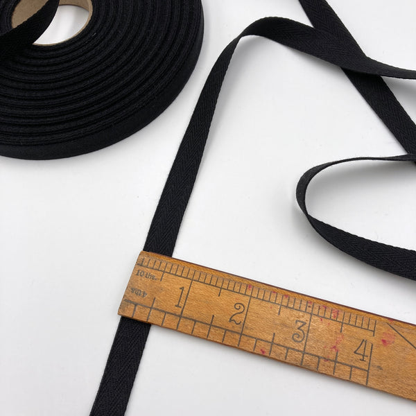 1/2" wide black twill tape laying on a white table with a ruler to show the scale.