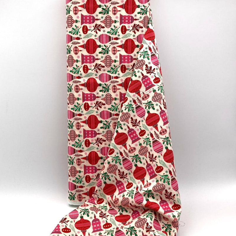 A bolt of ivory fabric with red and pink ornaments and mistletoe printed on it.