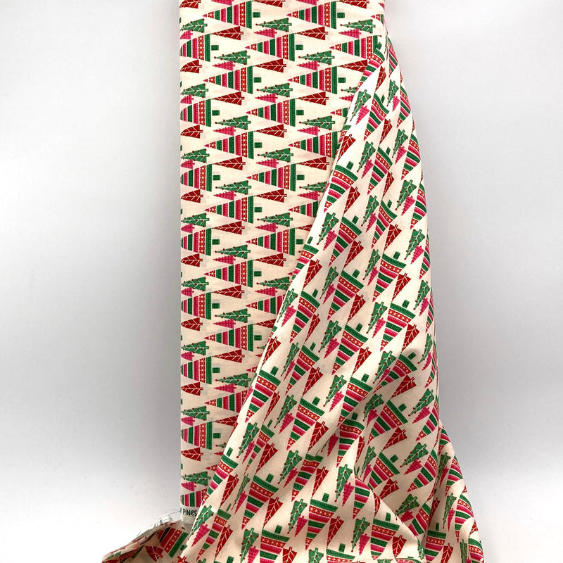 A bolt of off-white fabric with green, red, and pink trees printed on it. The bolt sits in front of a white backdrop.