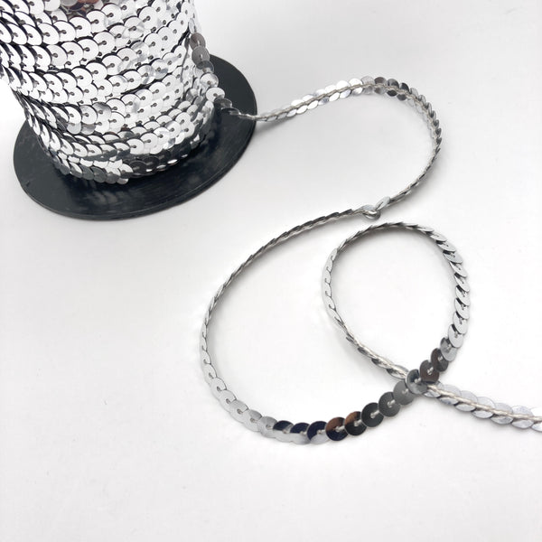 A roll of bright metallic silver sequin trim laying on a white table