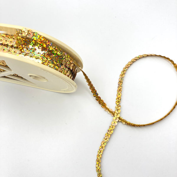 A roll of holographic gold sequin trim on a white backdrop