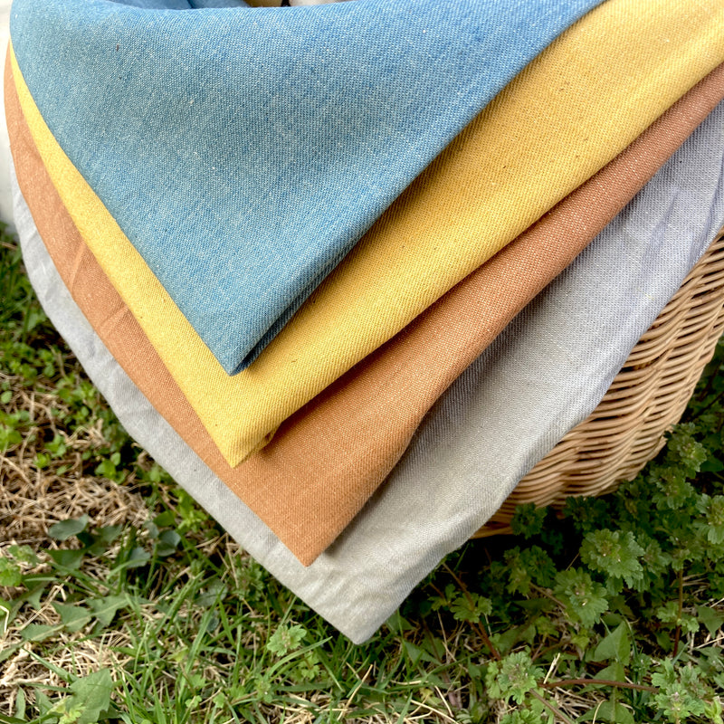 four colors of denim fabric folded and peeking out of a wicker basket atop green grass