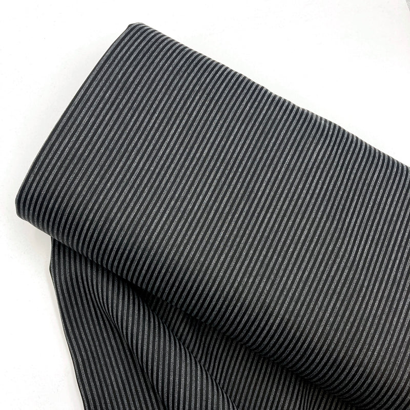 A bolt of charcoal grey and black striped fabric laying on a white backdrop.