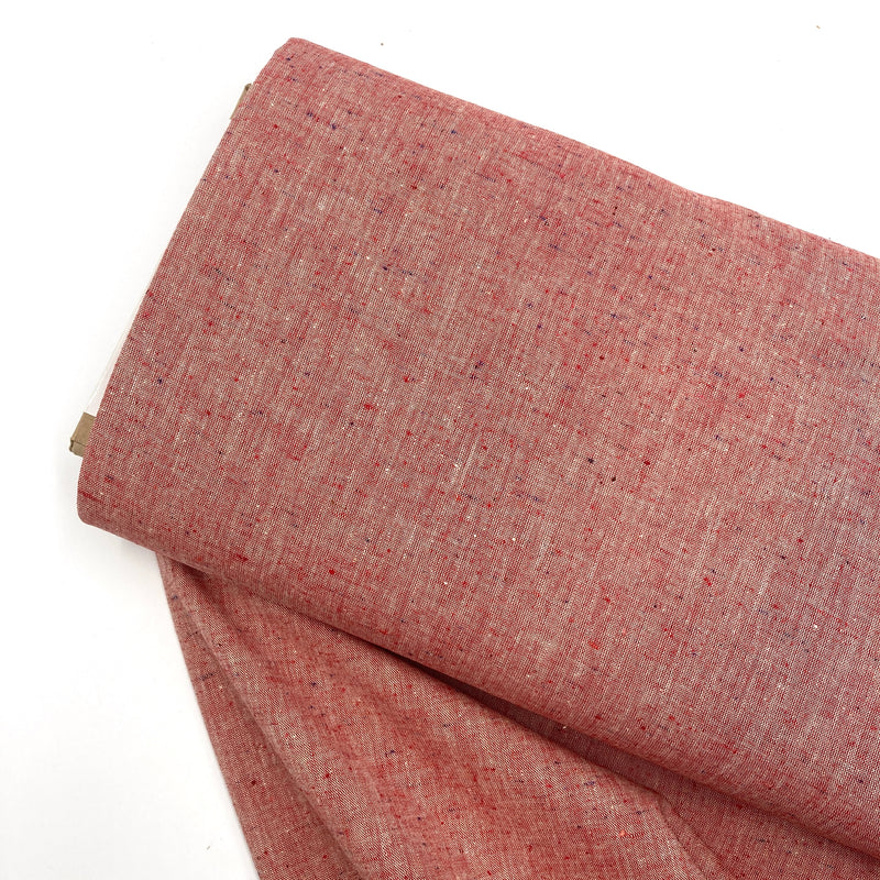 A bolt of red speckled chambray fabric lays on a white table