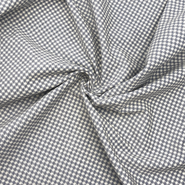 A photo of grey and white houndstooth corduroy fabric scrunched in a swirl to show its texture and thickness
