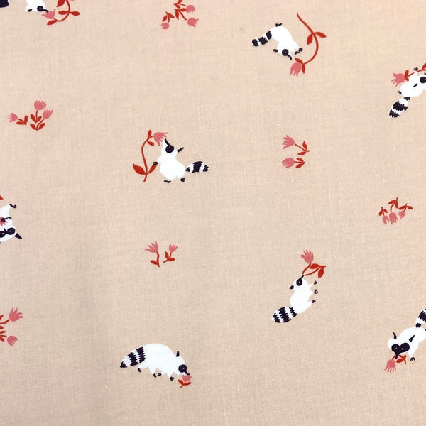 a peach fabric with small white raccoons sniffing pink flowers