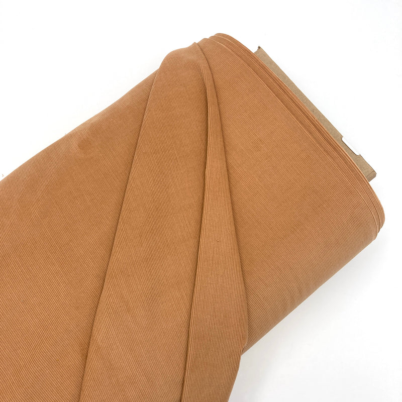 A bolt of golden brown corduroy fabric laying on a white backdrop
