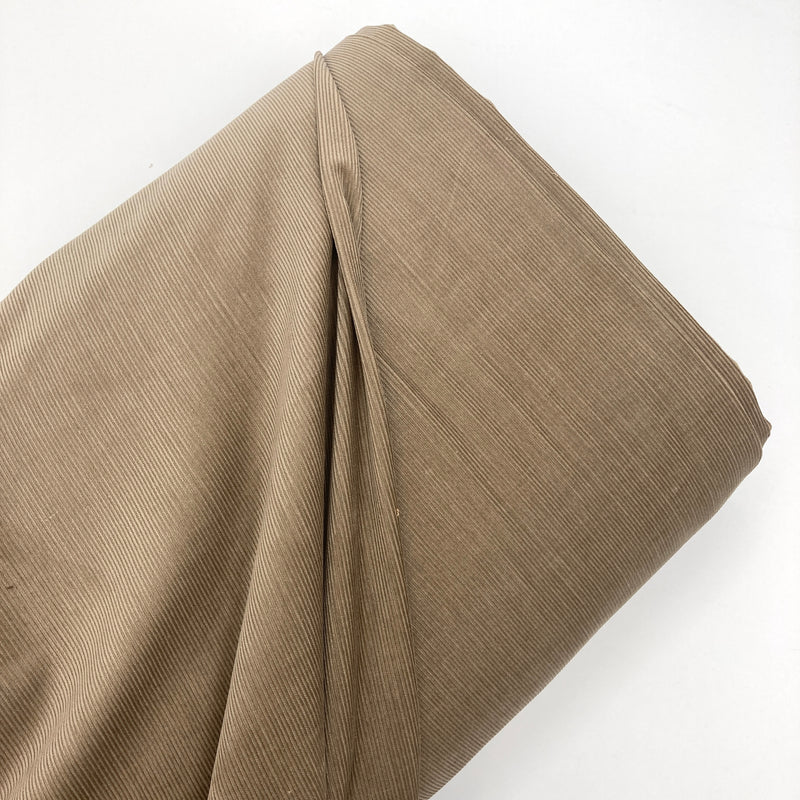 A bolt of mushroom-colored corduroy fabric laying on a white backdrop