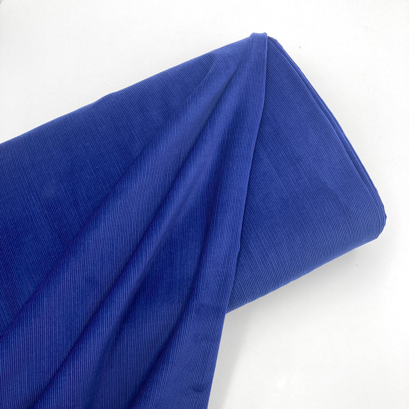 a bolt of bright cobalt blue corduroy fabric laying on a white background