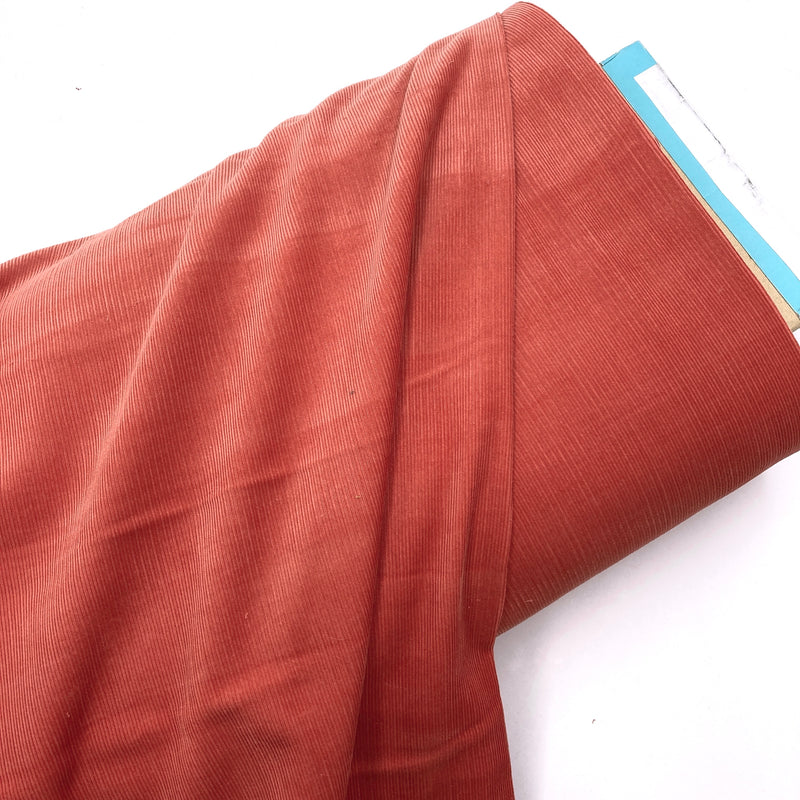A bolt of warm red corduroy fabric laying on a white backdrop