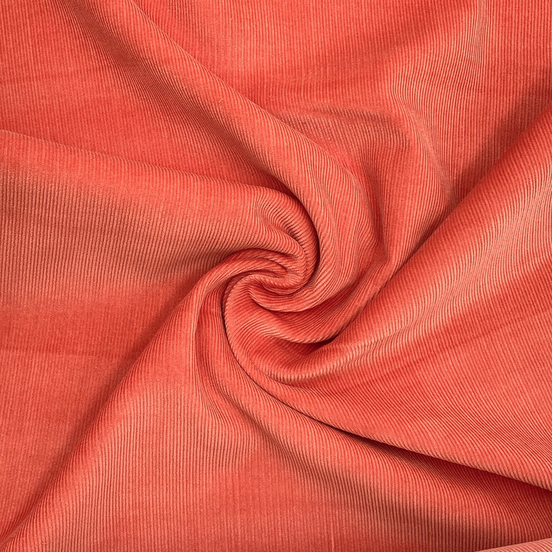 A warm red corduroy fabric scrunched in a swirl pattern to better show its texture and thickness
