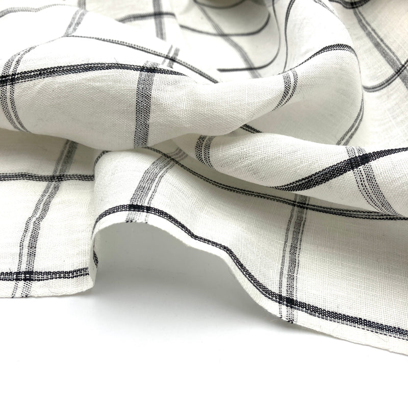 A close-up of white linen fabric with a black plaid windowpane design.