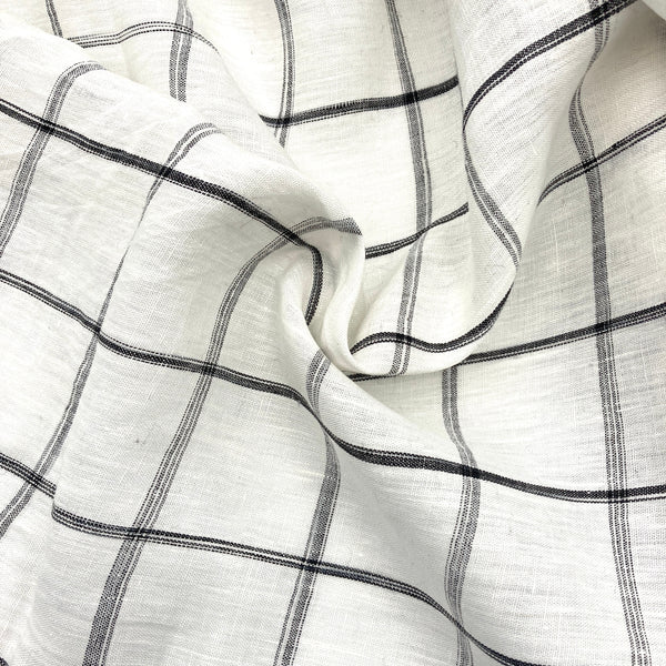 white linen fabric scrunched on a table to show its texture. It has a black windowpane plaid design on it.